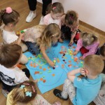 Powiększ zdjęcie Dzieci siedzą na podłodze w kole na środku leży niebieski plakat który ozdabiają