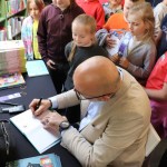 Powiększ zdjęcie Autor podpisuje książki dzieciom