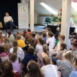 Powiększ zdjęcie Dzieci siedzą na podłodze w bibliotece i słuchają autora książek