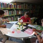 Powiększ zdjęcie Dzieci siedzą przy stolikach i wykonują pracę plastyczną