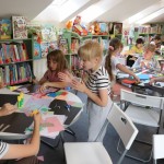 Powiększ zdjęcie Dzieci siedzą przy stolikach i wykonują pracę plastyczną