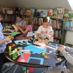 Powiększ zdjęcie Dzieci siedzą przy stolikach i wykonują pracę plastyczną