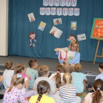 Powiększ zdjęcie Dzieci siedzą na podłodze w bibliotece i rozmawiają z panią