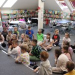 Powiększ zdjęcie Dzieci siedzą na podłodze w bibliotece i rozmawiają z panią