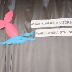 Powiększ zdjęcie Na szarym tle napis czterdziesty piąty konkurs recytatorski warszawska syrenka obok różowy rybi ogon