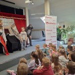 Powiększ zdjęcie Dzieci siedzą na podłodze w bibliotece i oglądają przedstawienie