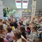 Powiększ zdjęcie Dzieci siedzą na podłodze w bibliotece i oglądają przedstawienie