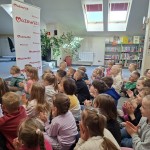 Powiększ zdjęcie Dzieci siedzą na podłodze w bibliotece i oglądają przedstawienie