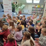 Powiększ zdjęcie Dzieci siedzą na podłodze w bibliotece i oglądają przedstawienie