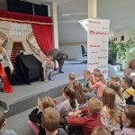 Powiększ zdjęcie Dzieci siedzą na podłodze w bibliotece i oglądają przedstawienie