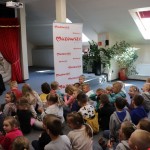 Powiększ zdjęcie Dzieci siedzą na podłodze w bibliotece i oglądają przedstawienie