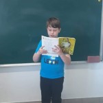 Powiększ zdjęcie Na zdjęciu uczeń przy tablicy czytający książkę