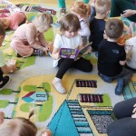 Powiększ zdjęcie Dzieci siedzą na dywanie i oglądają książki