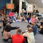 Powiększ zdjęcie Dzieci siedzą na podłodze w bibliotece i rozmawiają z panią
