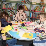 Powiększ zdjęcie Dzieci przy stoliku wycinają kwiatki z kolorowego papieru