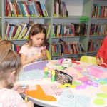 Powiększ zdjęcie Dziewczynki przy stoliku wycinają kwiatki z kolorowego papieru