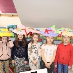 Powiększ zdjęcie Dziewczynki stoją w kapeluszach przy regale bibliotecznym