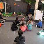 Powiększ zdjęcie Dzieci siedzą na dywanie w bibliotece bibliotekarka czyta test