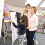 Powiększ zdjęcie Dziewczynka wraz z bibliotekarką przykleja pasek zadania na flipczart pani robi zdjęcie