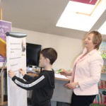 Powiększ zdjęcie Chłopiec wraz z bibliotekarką przykleja pasek zadania na flipczart