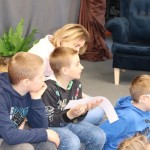 Powiększ zdjęcie Na zdjęciu trzech chłopców i pani jeden z nich czyta zadanie z paska kartki