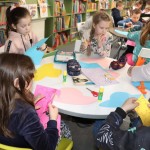 Powiększ zdjęcie Trzy dziewczynki przy stoliku wycinają kwiatki z kolorowego papieru