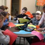Powiększ zdjęcie Chłopcy przy stolikach wraz z bibliotekarką wycinają kwiatki