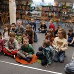 Powiększ zdjęcie Grupa dzieci siedzi na podłodze w bibliotece