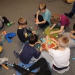 Powiększ zdjęcie Dzieci siedzą na podłodze i kleją pracę plastyczną