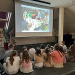 Powiększ zdjęcie Dzieci siedzą na podłodze i oglądają prezentację filmową
