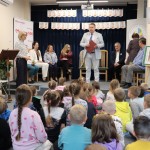Powiększ zdjęcie Dzieci siedzące tyłem i osoby dorosłe na scenie